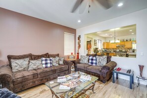A living room with two brown sofas, a glass coffee table with magazines, and a view into the kitchen. - Backyard Billiards & BBQ! Surprise Desert Stay (Surprise)