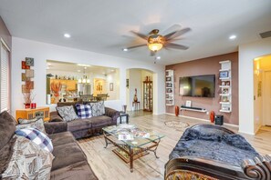 A living room with a sofa, a coffee table, and a television. There is a ceiling fan and recessed lighting. - Backyard Billiards & BBQ! Surprise Desert Stay (Surprise)