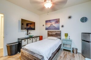 A modern bedroom with a bed, a TV, a painting, a clock, and a small table with a lamp. - Backyard Billiards & BBQ! Surprise Desert Stay (Surprise)