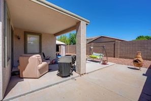 A covered patio area with a beige sofa, a covered exercise bike, and a swing set. - Backyard Billiards & BBQ! Surprise Desert Stay (Surprise)