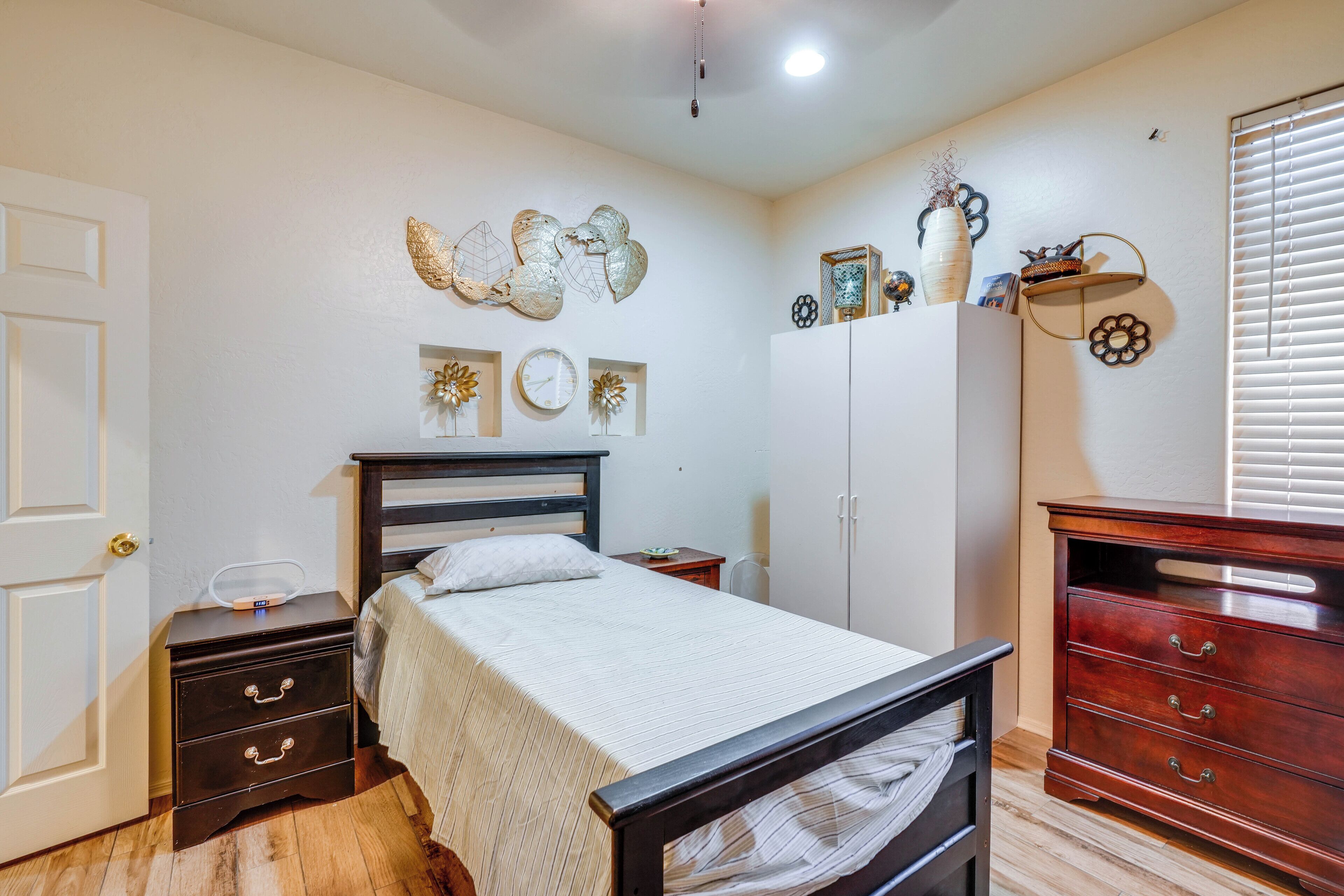A bedroom with a bed, a dresser, a nightstand, a wall clock, and decorative wall art.