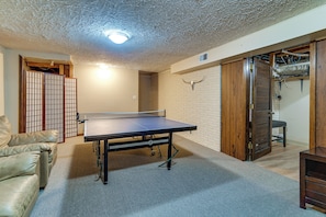 Une pièce avec une table de ping-pong, un canapé, une porte avec un cadre en bois et un luminaire au plafond.