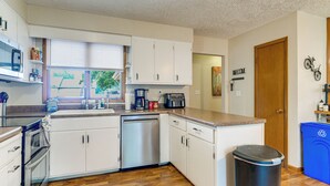 Cocina compacta con gabinetes blancos, lavavajillas, cafetera y un cubo de basura.
