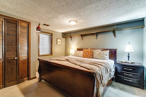A bedroom with a wooden bed, a nightstand with a lamp, a dresser, and a closet with sliding doors. - 7 Mi to Memorial Stadium! Group Retreat w/ Yard (Lincoln)