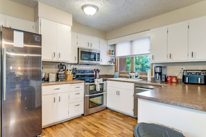 A modern kitchen with stainless steel appliances, white cabinetry, and a wooden floor. - 7 Mi to Memorial Stadium! Group Retreat w/ Yard (Lincoln)
