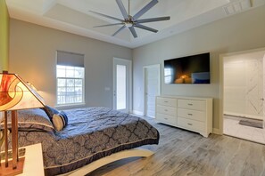 Een slaapkamer met een bed, een plafondventilator, een dressoir, een televisie en een deur.