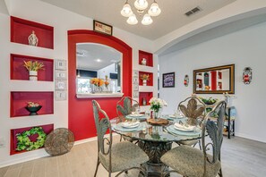 A dining area with a red accent wall, a chandelier, and a mirror. - 9 Mi to Disney! Family-Friendly Home w/ Pool (Kissimmee)