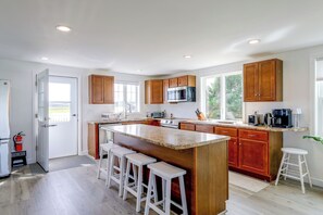 A modern kitchen with a central island, wooden cabinets, and a stainless steel microwave. - 1 Mi to Plum Island Beach with Beautiful Views (Newbury)