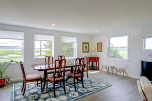 A dining area with a wooden table and chairs, a rug, and large windows with a view of greenery. - 1 Mi to Plum Island Beach with Beautiful Views (Newbury)