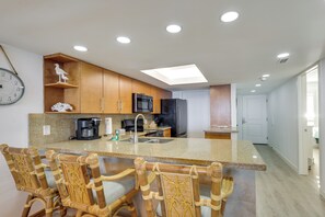 Una cocina moderna con una isla central, sillas de madera, cafetera y microondas.
