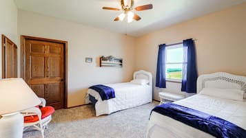 Une chambre avec deux lits, un ventilateur de plafond, une fenêtre avec des rideaux et une porte.