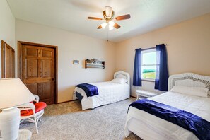Una habitación con dos camas, ventilador de techo, ventana con cortinas y una puerta.