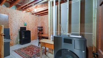 A room with a large washing machine, a wooden table, a chair, and a television on a stand.