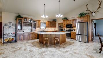 A spacious kitchen with a central island, wooden cabinets, stainless steel appliances, and a ceiling fan.