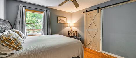 A bedroom with a bed, a ceiling fan, a window with curtains, a wall-mounted lamp, and a sliding barn door.
