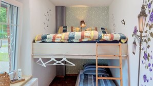 Ein kleines Zimmer mit Etagenbett, einem Tisch mit Korb und einem Heizkörper.