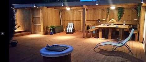 Un patio al aire libre con cubierta de madera, una mesa redonda, un sillón de descanso y una mesita con una planta.