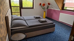 Un dormitorio con cama, una mesita, una silla, un ventanal con vistas y un florero con flores.