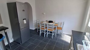 A compact kitchen with a refrigerator, a dining table with chairs, and a black countertop.