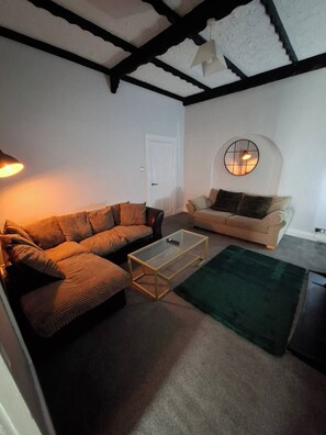 A living room with a sectional sofa, a smaller sofa, a glass coffee table, and a green rug.