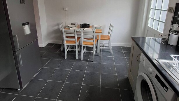 A kitchen with a dining table, chairs, a clock, a washing machine, and a refrigerator.