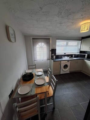 A compact kitchen with a dining area, a washing machine, and a window with blinds.