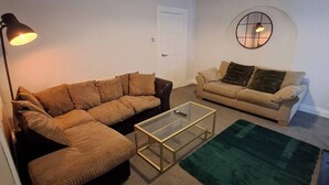 A living room with two sofas, a glass coffee table, a green rug, and a ceiling with exposed beams.