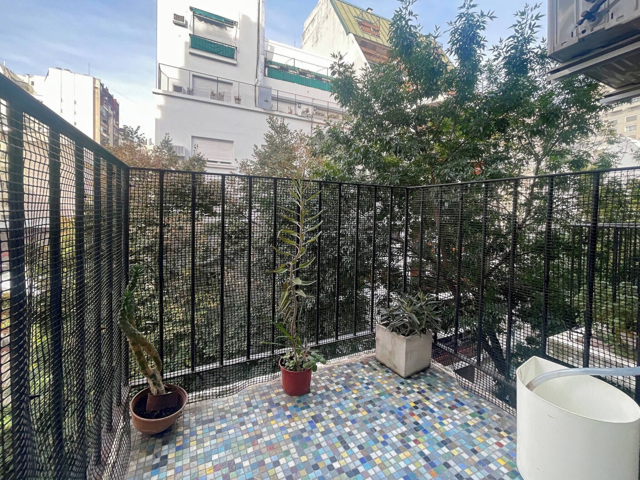 Een balkon met betegelde vloer, plantenpotten en een gaashek.