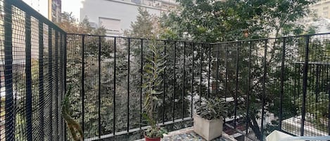 Un balcon doté d’un sol carrelé, de plantes en pot et d’une clôture en treillis métallique.