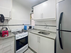 Una cocina compacta con armarios blancos, estufa a gas, microondas, lavaplatos y refrigerador.