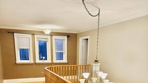 A spacious room with a wooden staircase, a chandelier, and a view of the outdoors through windows.
