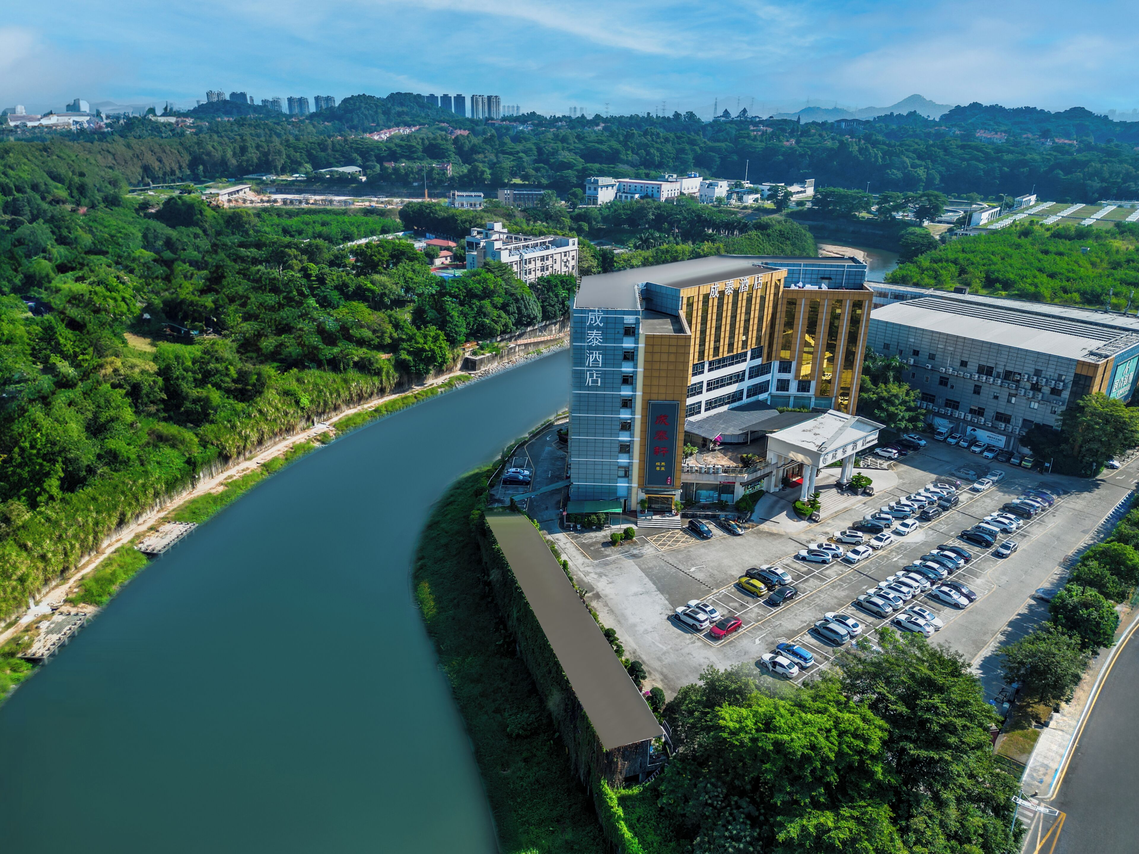 A hotel with a parking lot, a river, and surrounding greenery.