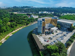 A hotel with a parking lot, a river, and surrounding greenery.