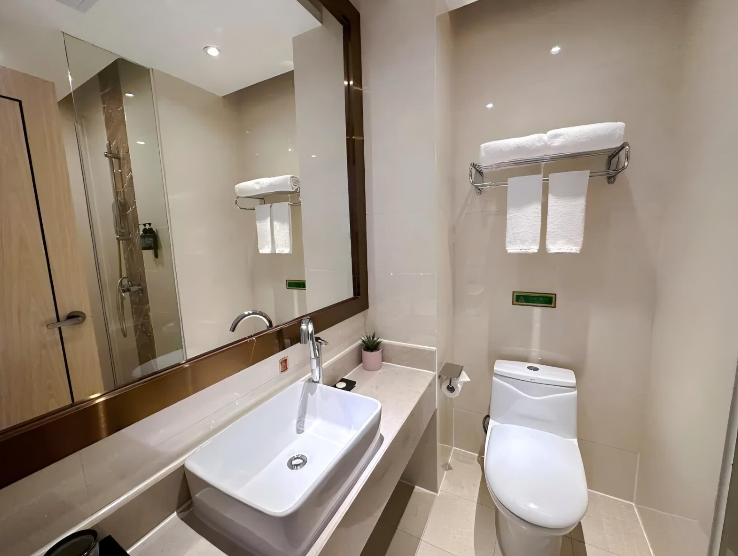 A modern bathroom with a large mirror, a sink, a toilet, and a towel rack.