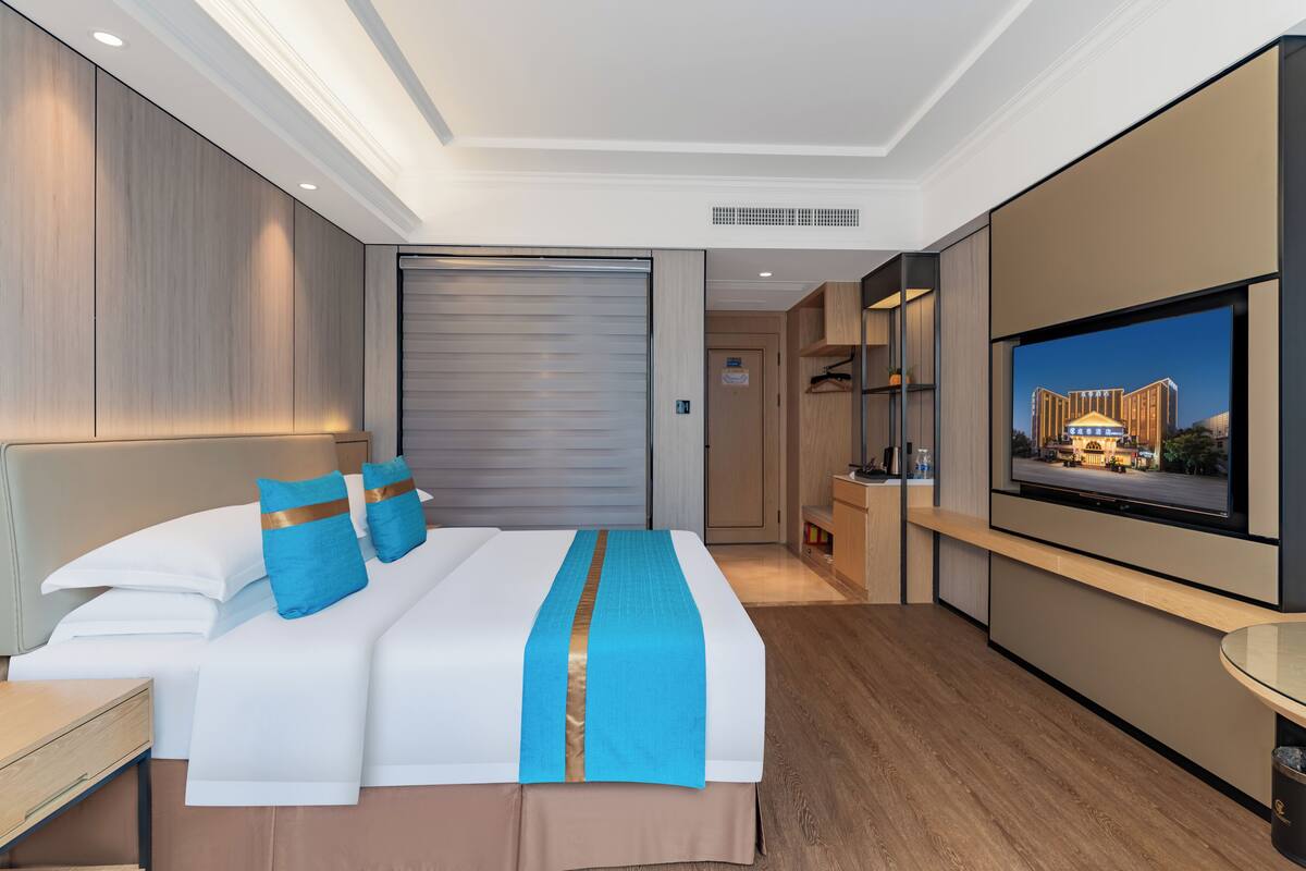 Ein modernes Hotelzimmer mit einem großen Bett, einem Flachbildfernseher, Holzboden und Blick auf ein Gebäude.