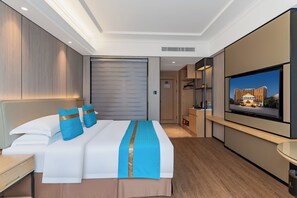 A modern hotel room with a large bed, a flat-screen TV, a wooden floor, and a view of a building outside.