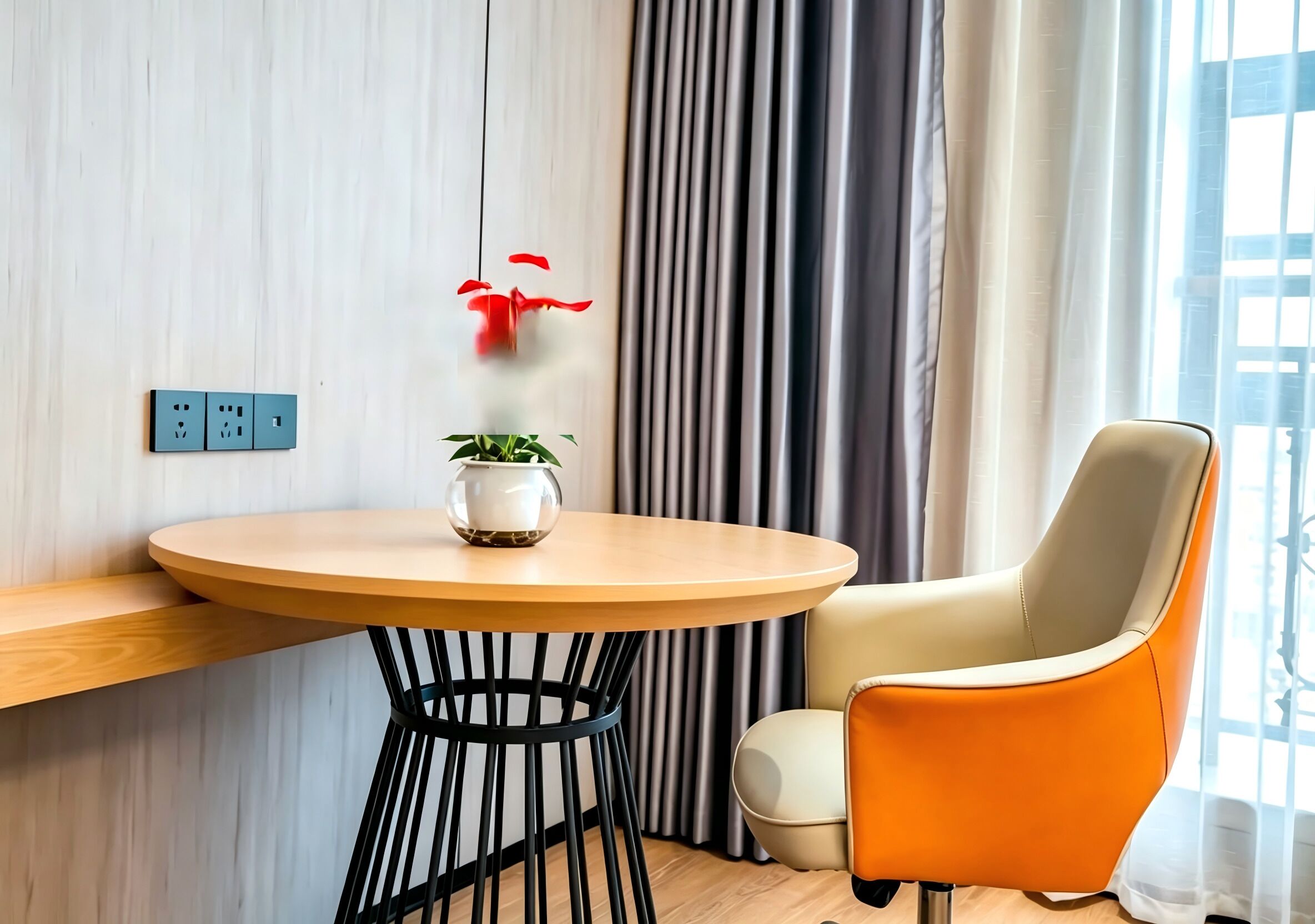 Habitación moderna con una mesa redonda de madera, una planta en maceta, una flor roja, una silla y un enchufe.