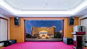 Un vestíbulo de hotel con alfombra roja, un escenario y un amplio ventanal con vistas al exterior del hotel.