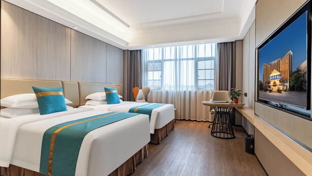 Habitación de hotel con dos camas, una mesita, una silla, un televisor y un ventanal con cortinas.