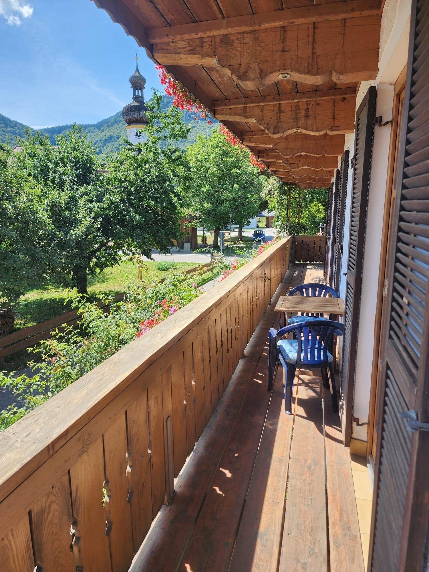 Un balcon en bois offrant une vue sur le clocher d’une église et sur une végétation luxuriante.