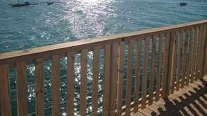 Een houten terras met uitzicht op een rustige zee en bootjes.