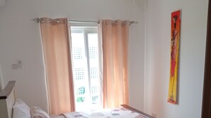 Een slaapkamer met een bed, gordijnen, een raam en een kunstwerk aan de muur.