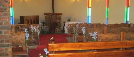 A church interior with wooden pews, a red carpet aisle, a wooden pulpit, and a cross on the wall.
