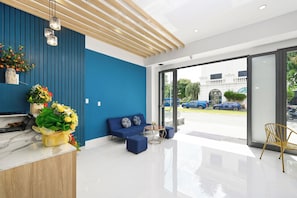 A modern reception area with a blue wall, a reception desk, a blue sofa, and a chair. - Arina Hotel 3 (Tan Ninh)