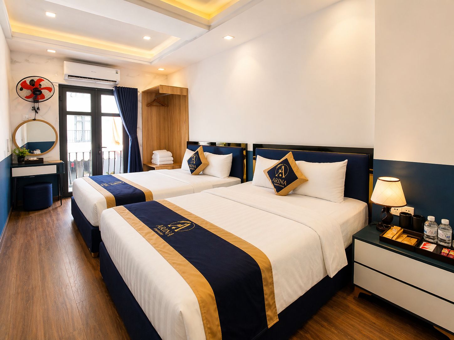 A hotel room with two beds, a desk, a chair, an air conditioning unit, and a window with curtains.