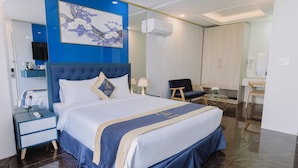 A hotel room with a large bed, a desk, a chair, a television, and a painting on the wall.