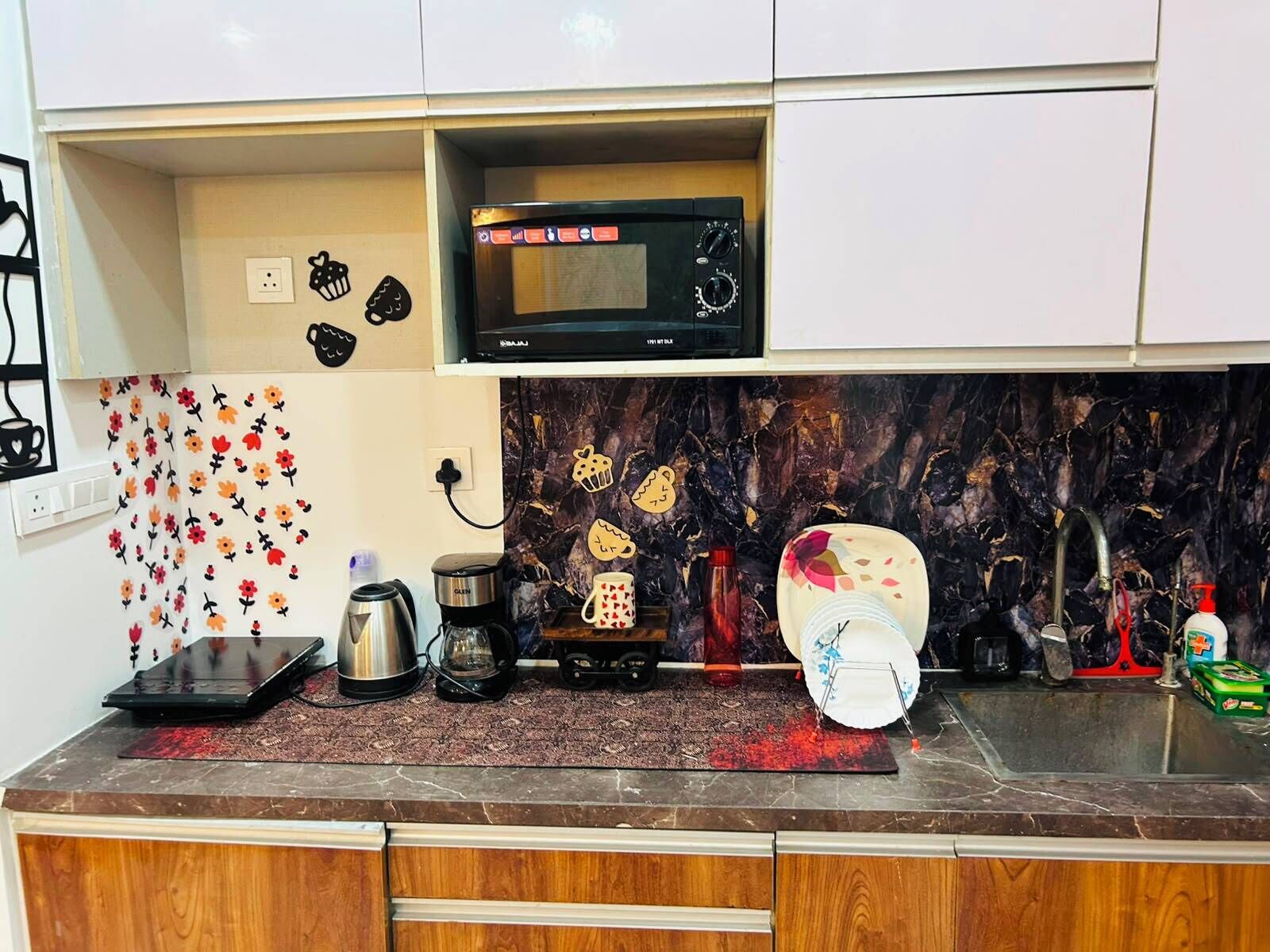 Een keuken met een magnetron, koffiezetapparaat, waterkoker en een spoelbak met kraan.