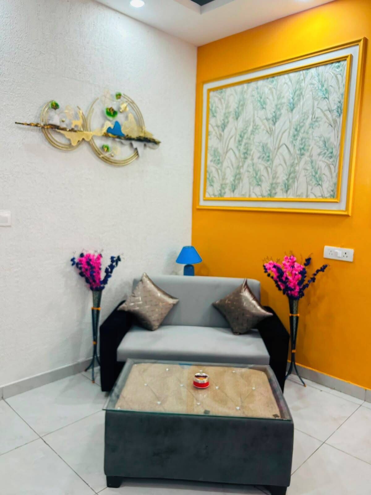 A living room with a sofa, a coffee table, decorative wall art, and two vases with flowers.