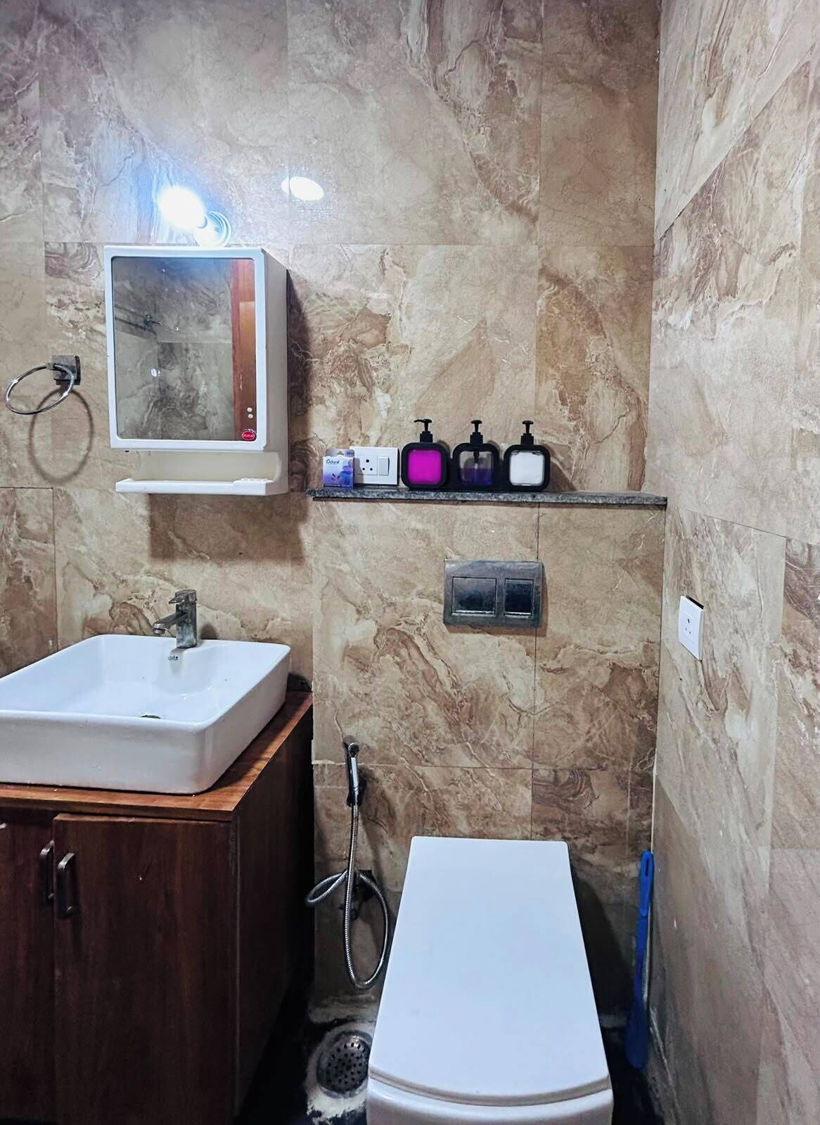 Un baño con lavamanos blanco, un espejo, un estante con dispensadores de jabón, ducha e inodoro.
