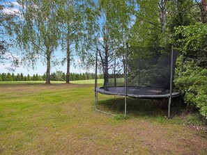 Un trampolín en un campo cubierto de césped, con árboles al fondo.